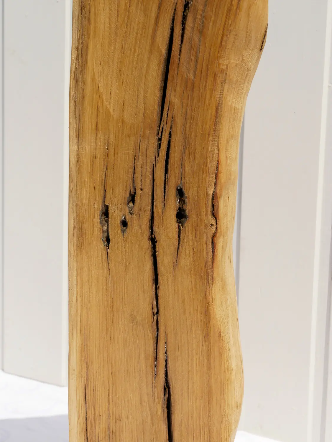 Aufnahme einer rustikalen Eichenholz-Skulptur mit tiefen Maserungen und natürlichen Verwitterungsspuren. Das Holz ist hellbraun und steht fest auf einem flachen, quadratischen, schwarzen Metallsockel. Nachhaltig und handgefertigt.